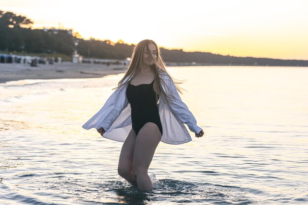 夕暮れ時の海で水着と白いシャツを着た女性