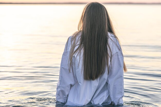 A woman in a swimsuit and a white shirt in the sea at sunset