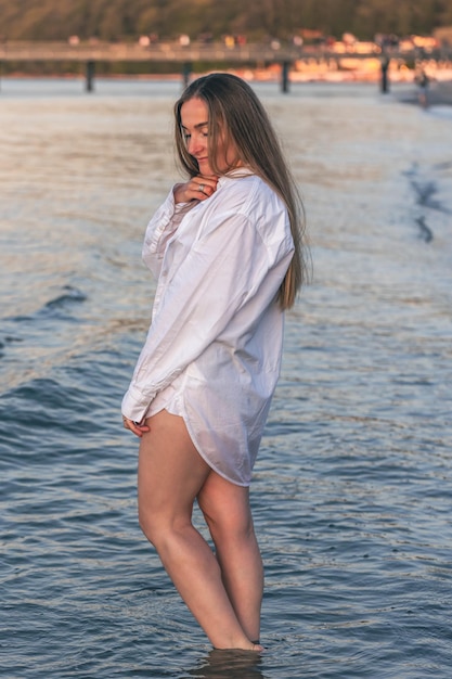 A woman in a swimsuit and a white shirt in the sea at sunset