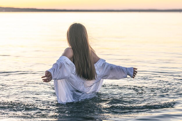 A woman in a swimsuit and a white shirt in the sea at sunset