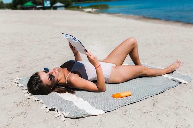 Free photo woman in swimwear reading book on beach