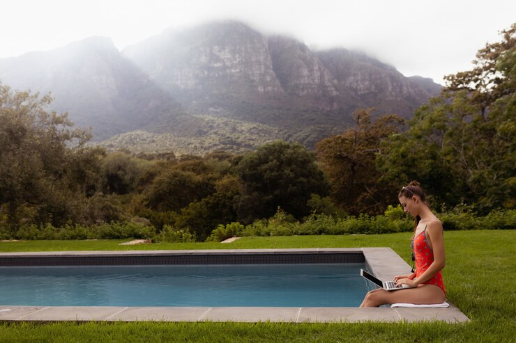 Free Photo woman in swimwear using laptop near poolside in the backyard