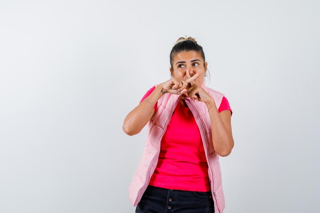 Woman in t-shirt, vest crossing fingers forming an x on mouth and looking focused 