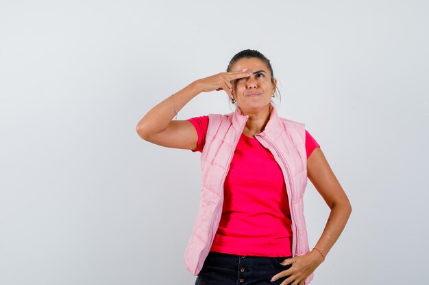 Woman in t-shirt, vest keeping fingers on eye and looking charming 