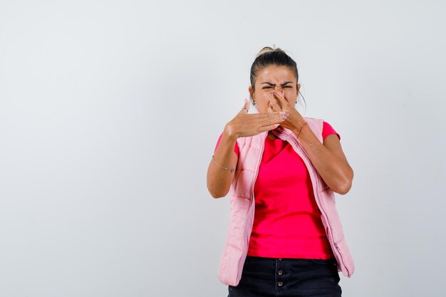 Woman in t-shirt, vest pinching nose due to bad smell and looking disgusted 