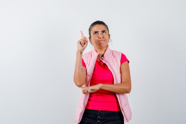 Woman in t-shirt, vest pointing up and looking serious 