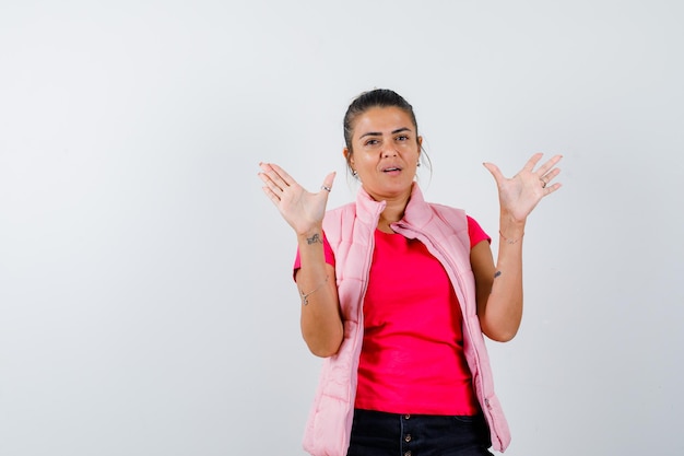 Woman in t-shirt, vest showing empty palms and looking confident 