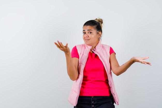 Woman in t-shirt, vest showing helpless gesture and looking confused 