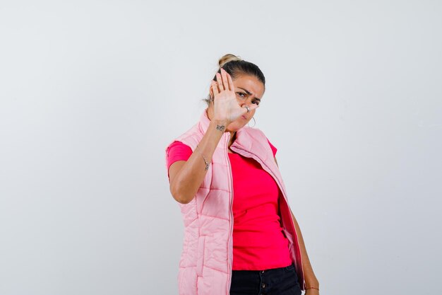 Woman in t-shirt, vest showing stop gesture and looking annoyed 