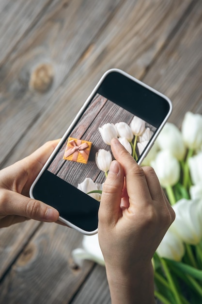 Woman take picture of bouquet of white tulips and gift box