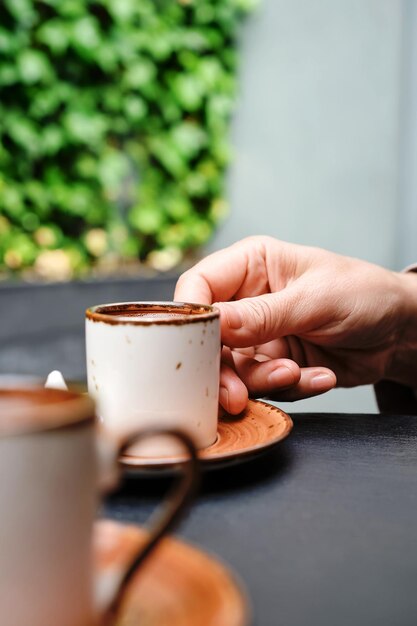 A woman takes a cup of coffee Turkish black frothy coffee on a black stone table with branches of wild ivy in the background Vertical frame selective focus