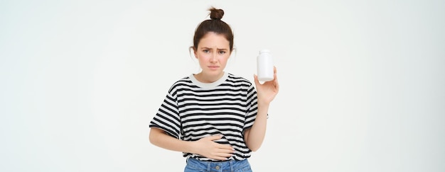 Free photo woman takes painkillers pills from stomach ache menstrual pain holds hand on belly shows bottle with