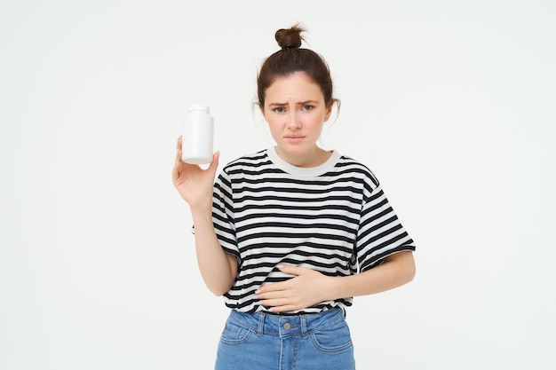 Woman takes painkillers pills from stomach ache menstrual pain holds hand on belly shows bottle with