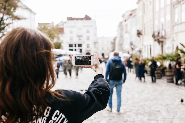 女性、スマートフォンで市街広場の写真を撮る