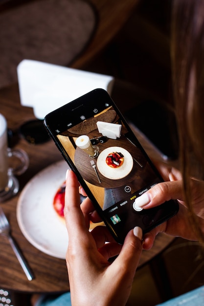 Женщина фотографирует десерт на своем смартфоне