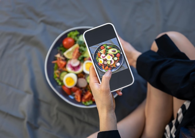 A woman takes a photo of fresh vegetable salad on a smartphone