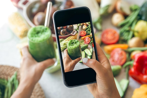Free photo a woman takes a photo of a vegetable smoothie on smartphone a blogger takes a photo of food the concept of weight loss and detox