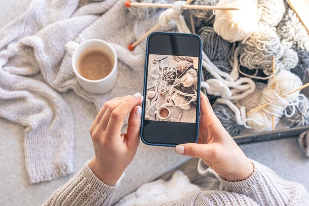 女性がスマートフォンで糸の糸とコーヒーを写真に撮る