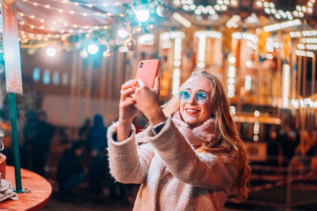 여자는 저녁 거리에서 defocus 배경 빛에 selfie를 걸립니다.