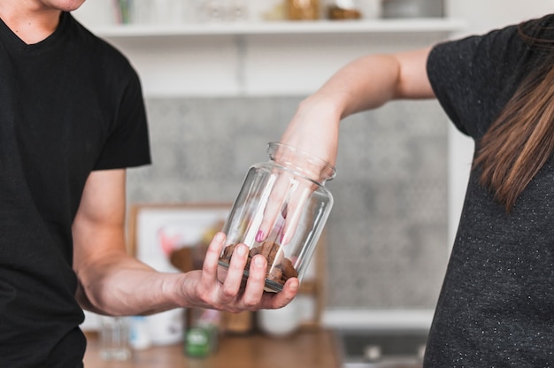 Woman taking cookies from glass jar hold by a man