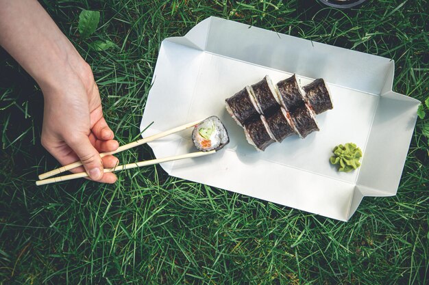 Donna che cattura delizioso maki roll dal piatto su sfondo di erba