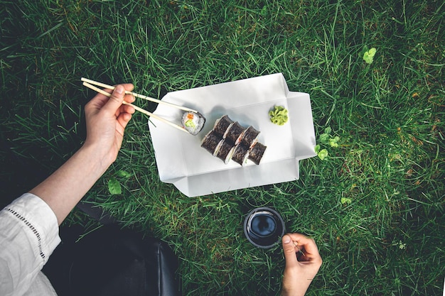 Free photo woman taking delicious maki roll from plate on grass background