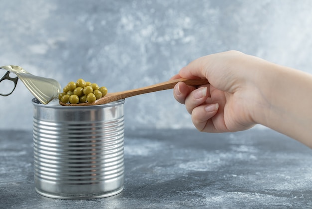 Free photo woman taking green peas from tin with spoon over grey table.