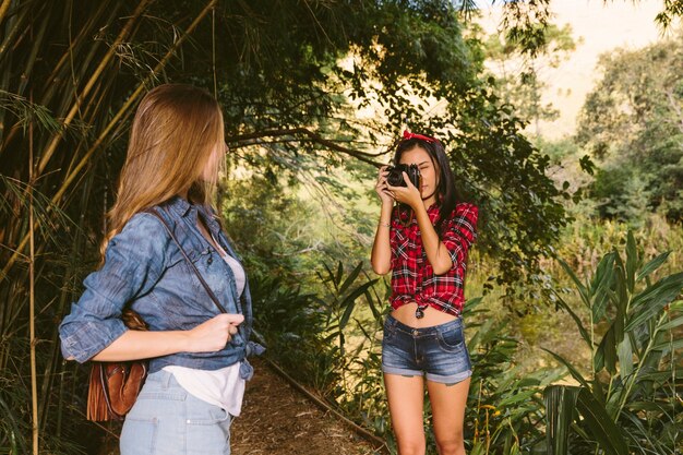 Woman taking her friends photograph with camera in forest