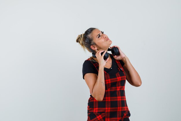 Woman taking off headphones in pinafore dress and looking dreamy. front view.