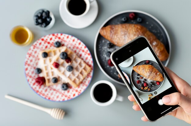 Woman taking photo of croissant with fruits