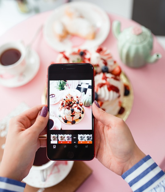 Woman taking a photo of pastry with berries on smartphone