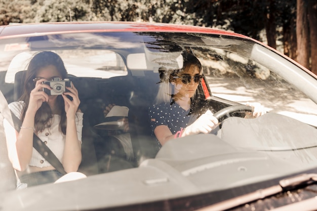 차에서 그녀의 친구와 함께 여행하는 동안 카메라로 사진을 복용하는 여자