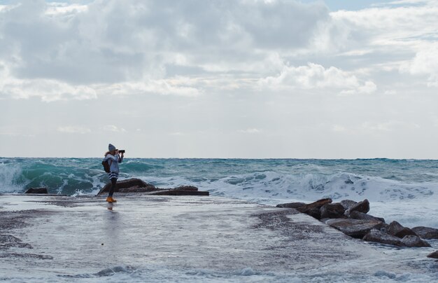 woman taking photo with camerin beach during daytime with sea