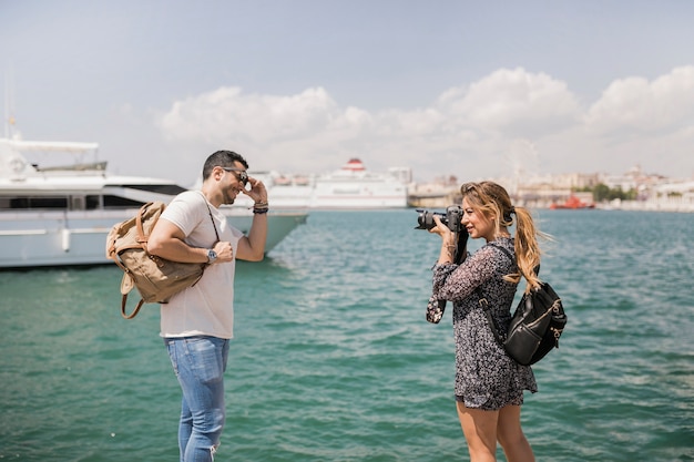 海の近くのカメラで彼女のボーイフレンドの写真を撮っている女性