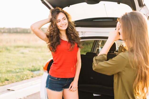 Woman taking picture of friend near car