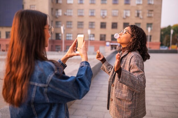 Woman taking pictures of her friend blowing bubbles outdoors