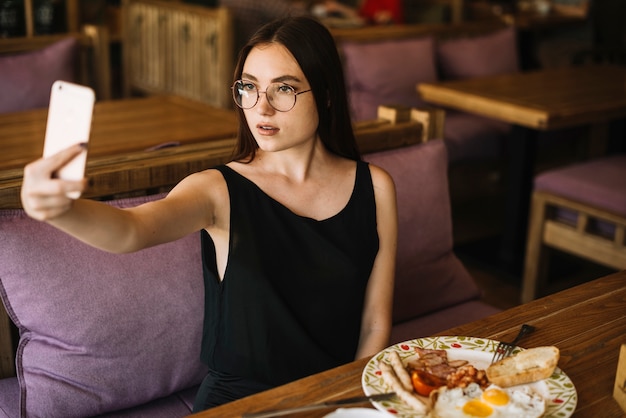 Woman taking selfie from cell phone sitting at caf���