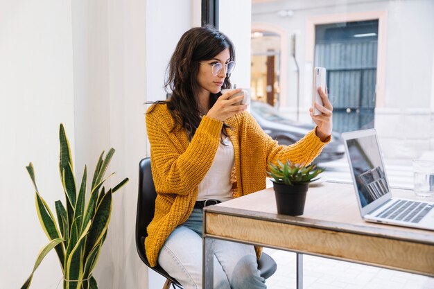 Woman taking selfie on smartphone in cafe