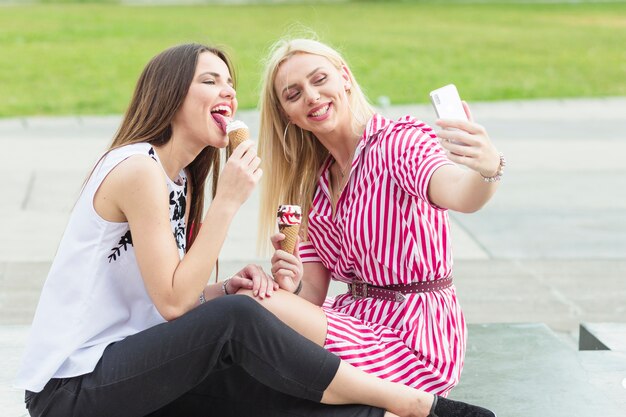 Woman taking selfie while her friend licking icecream with cellphone