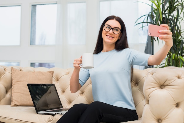 ソファでコーヒーを飲みながらselfieを取っている女性