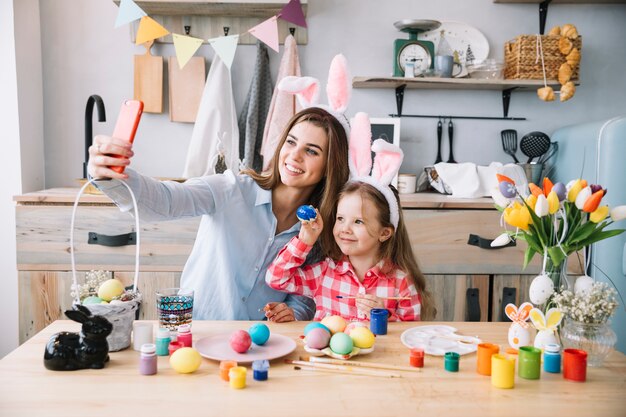 Woman taking selfie with daughter near Easter eggs 