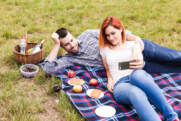 屋外のピクニックで彼女のボーイフレンドとセルフを取っている女性