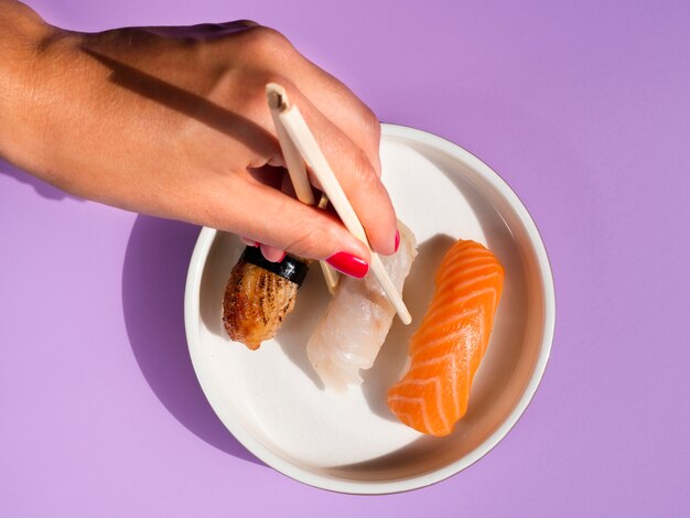 Woman taking a sushi from a white plate on blue background