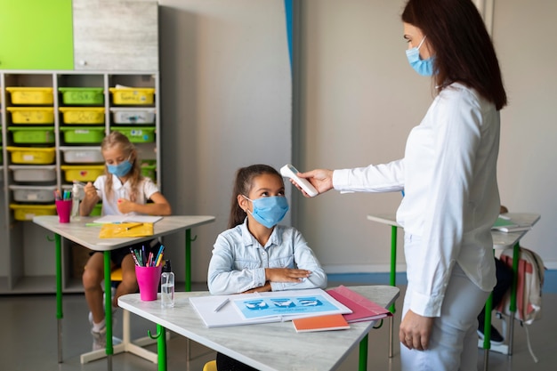 Woman taking the temperature of kids in the classroom