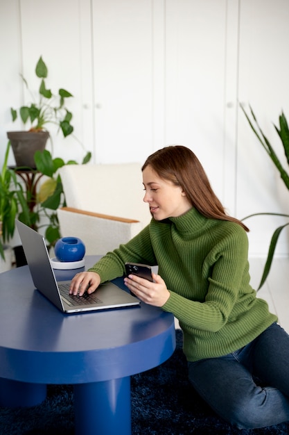 Woman talking on her smartphone using the handsfree feature and writing something on her laptop