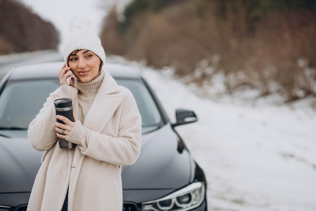 Woman talking on the phone by her car on the road in winter forest