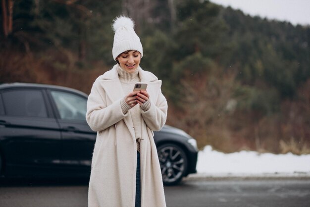 Woman talking on the phone by her car in winter forest