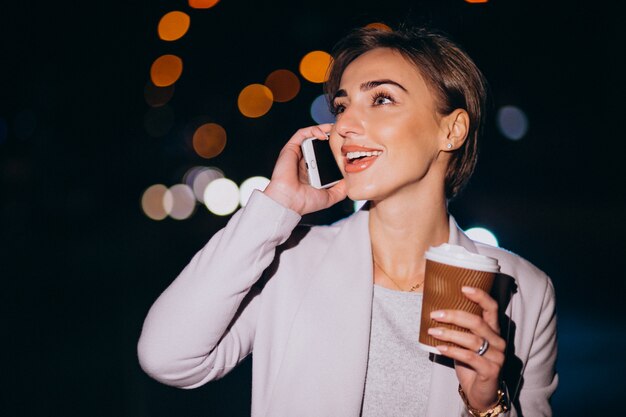 Donna parla al telefono e bere caffè fuori in strada di notte