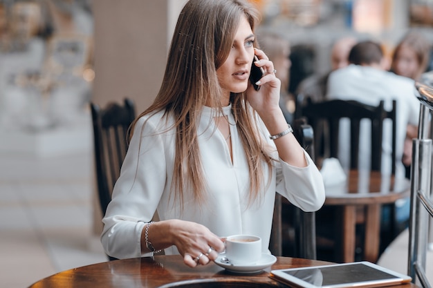 女電話で話し、コーヒーのカップを保持します