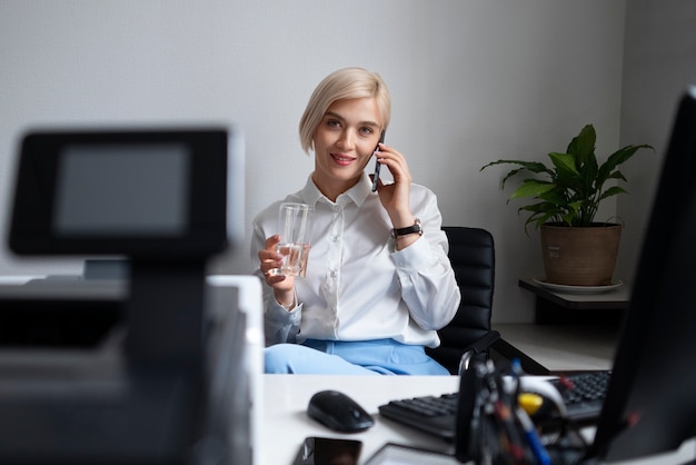 Foto gratuita donna che parla al telefono al lavoro accanto alla stampante